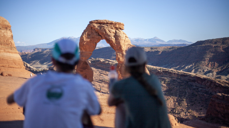Tourists crouch on the ground in front of a rock formations in Arches National Park.