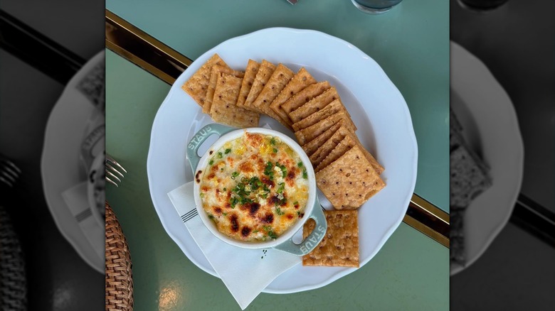 Plate of a cheesy dip with crackers on a green table.
