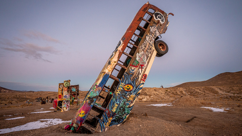 Graffiti-covered bus partially buried in desert