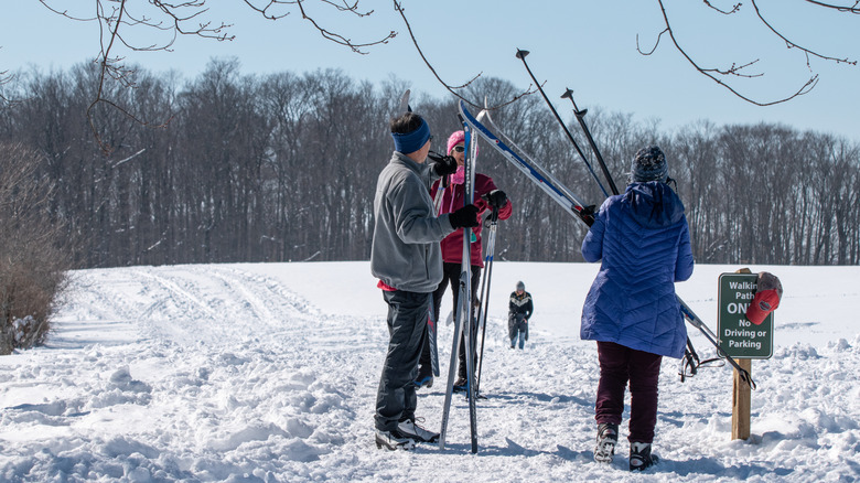 Skiiers rest at Knox Farm State Park, with a snowy field, bare trees, and a blue sky in the background