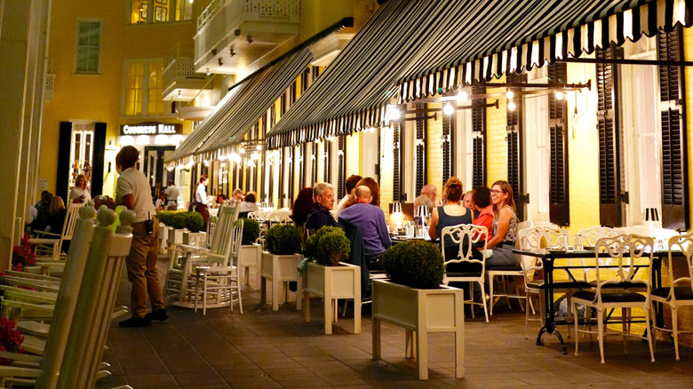 people sit at restaurant tables under awnings at Congress Hall, evening