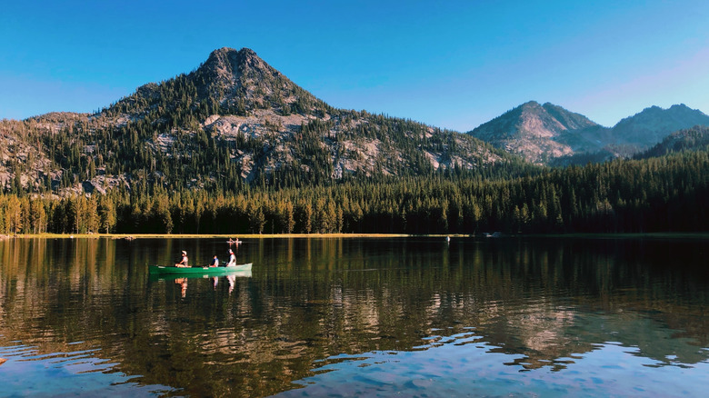 People in a canoe on Wallowa Lake with tree-dotted mountains in the background on a sunny clear sky day