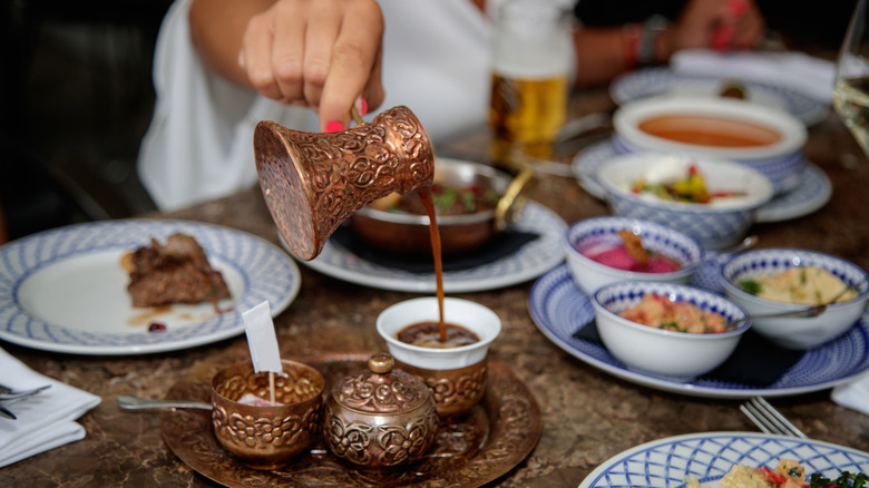 Turkish coffee being poured in foreground, with a Turkish food spread on blue and white plates in the background