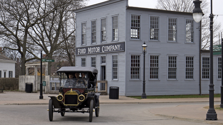 Replica Model T drives in front of a Ford Motor Company building in the Greenfield Village museum complex