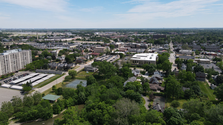 Aerial view of Dearborn, Michigan under a cloudy blue sky, with the Ford Motor Company world headquarters on the left and trees in the bottom of the frame