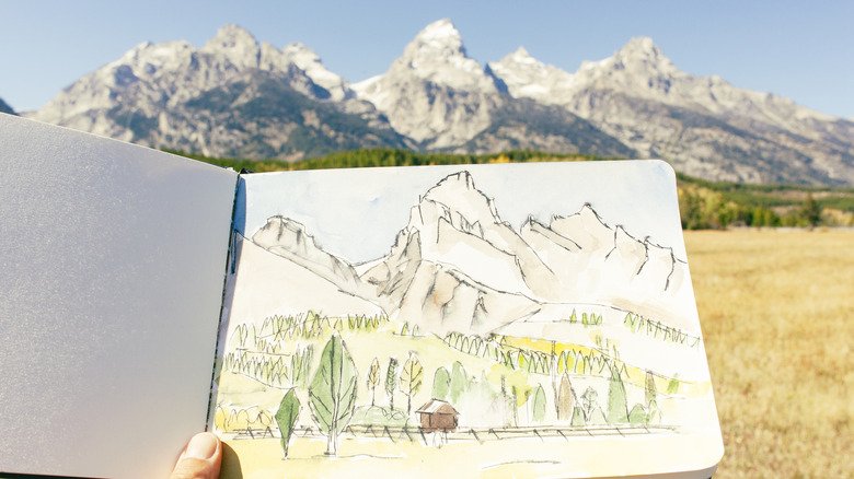 woman holds drawing inspired by grand teton mountains in background