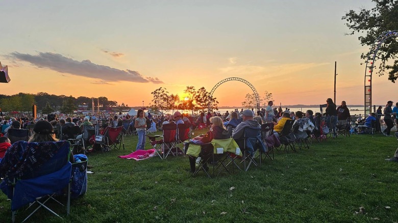 People sitting on lawn chairs in front of the lake and the sunset