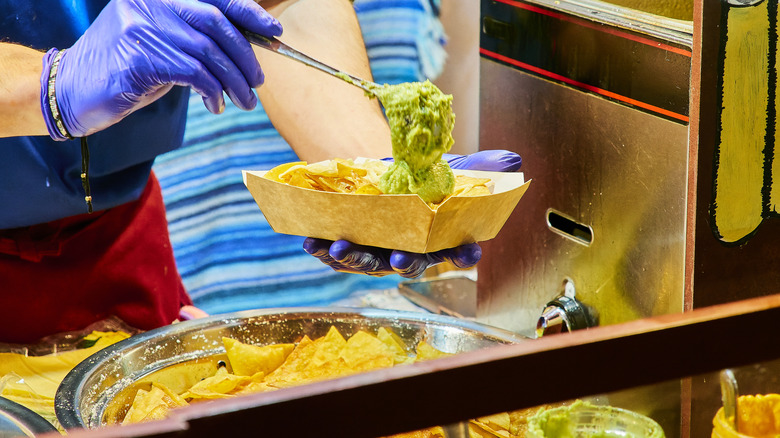 Gloved hands preparing nachos with guacamole