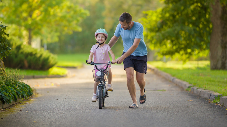 A father teaching his daughter how to ride a bike in a city park