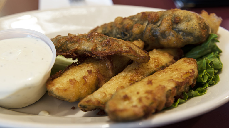 Plated fried pickles on a bed of lettuce with sauce