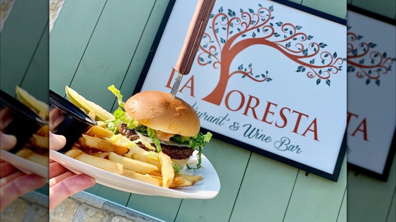 Person holding plate of burger and fries in front of La Foresta sign