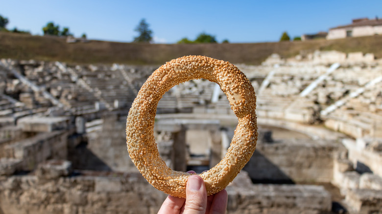 Circular Greek pastry held up over Larissa's ancient amphitheater