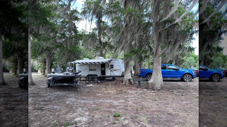 A blue pickup truck parked beneath cypress tress with an extra-long trailer and a motorized bass fishing boat at Lake Arbuckle