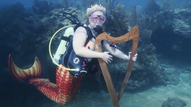 Scuba diver dressed as mermaids at the ocean floor playing a harp
