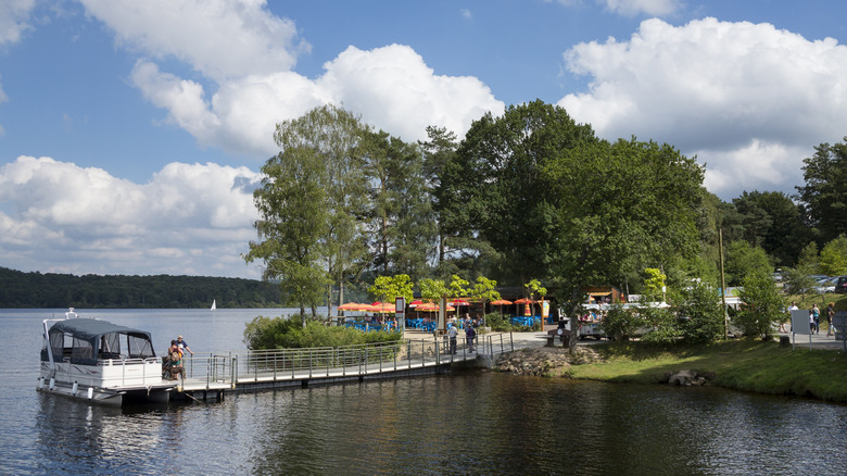 A long pier near tall trees and an outdoor restaurant leading out to a pontoon boat on Lac de Vassivière