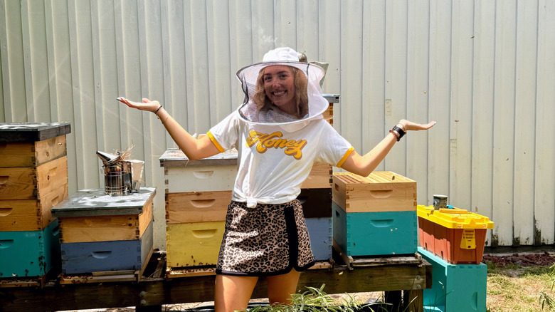 Author standing in front of bee boxes and wearing a bee vail