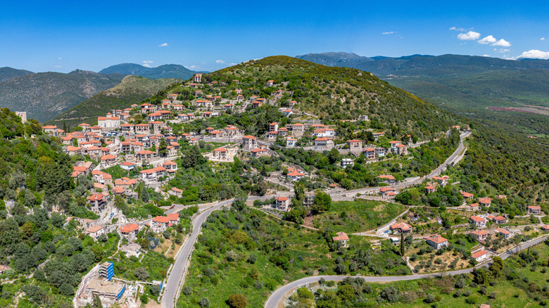 Aerial view of mountain village with stone houses and red tile roofs surrounded by lush mountains, Karytaina