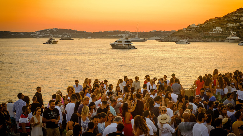A crowd forms near a lookout point at sunset on Mykonos