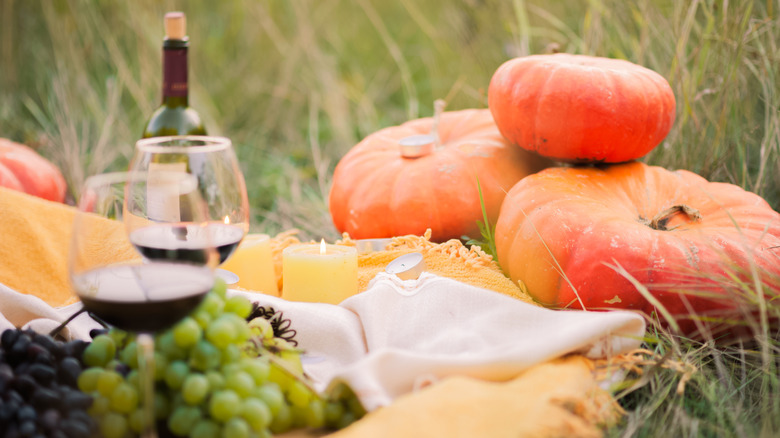 Picnic laid out with pumpkins, red wine, candles, and grapes