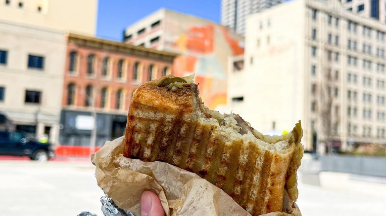 A woman holding a Subito sandwich with Indianapolis in the background