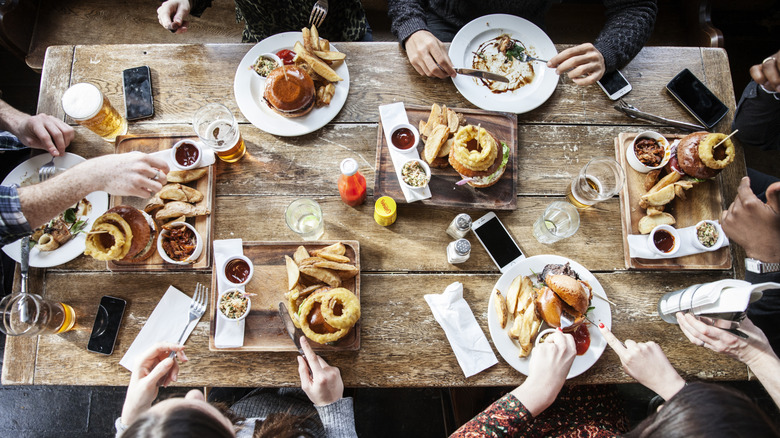 People eating burgers and fries and drinking beer at a dinner table