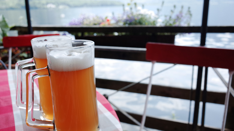 Two glasses of beer on a table by the lake.