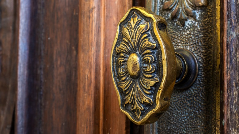 An ornate brass doorknob against wooden door