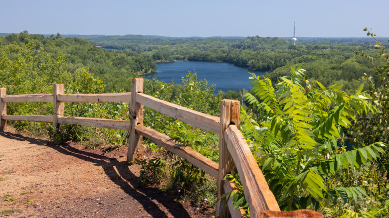 A trail with an overlook of a lake surrounded by trees