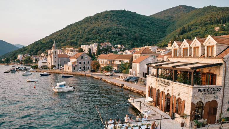Restaurants and historic buildings on Tivat seafront with forested mountains in the background