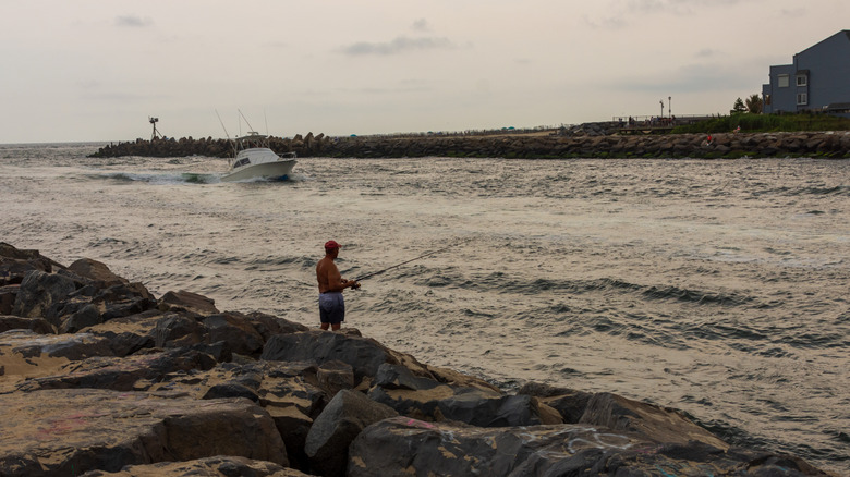 A boat in the inlet of Manasquan Beach, and someone fishing on the pier in the foreground