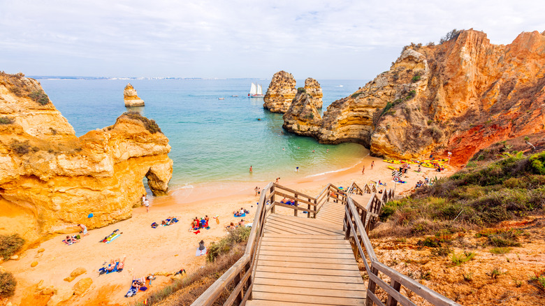 Wooden stairs leading down to a small beach flanked by golden sandstone cliffs