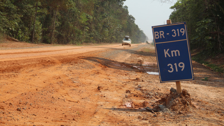 a sign marking the BR-319 on a dirt road with a car approaching in the background