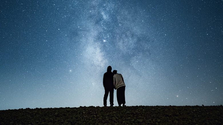 A couple holds hands under a brilliant night sky
