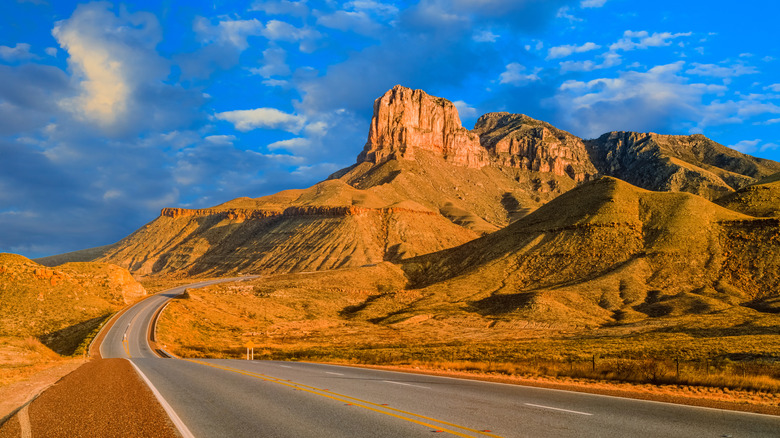 A paved road cuts through the desert and past a towering rock formation at Guadalupe Mountains National Park, in Texas.