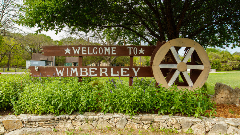 A rustic, wooden "Welcome to Wimberley" sign over a large wagon wheel in the Texas Hill Country