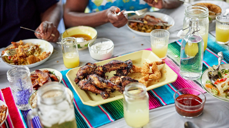 People gather around a table with jerk chicken and other food