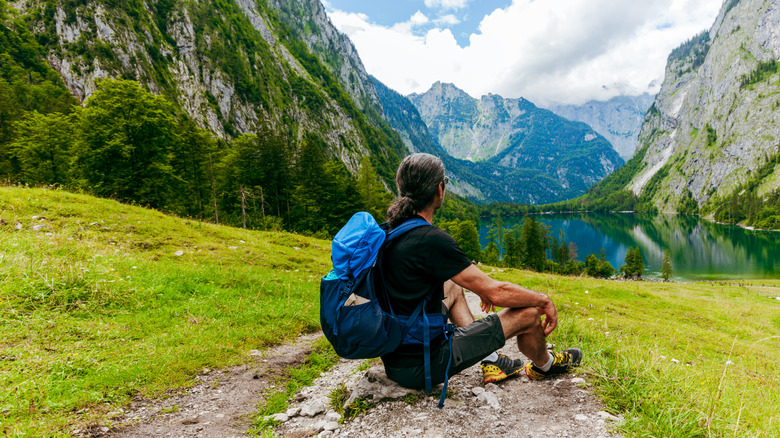 A hiker rests on a trail overlooking a lake above the Königssee in southern Germany