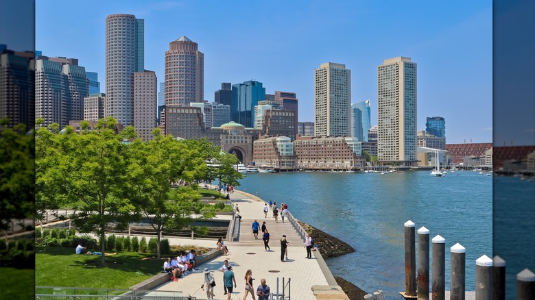 people walk on a waterfront path by the Boston Harbor