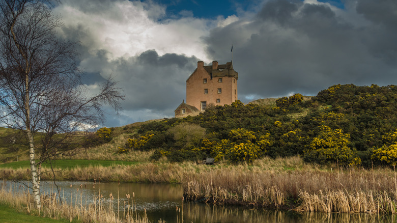 Fenton Tower on hilltop surrounded by dark clouds, bare trees, fields, and lake