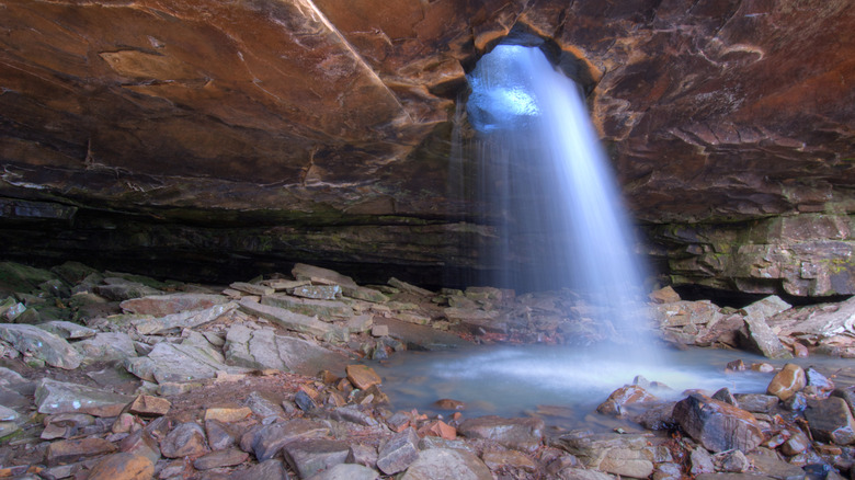 Sunlight and water streams through a hole in the cliffs at Glory Hole Waterfall in Ozark National Forest.