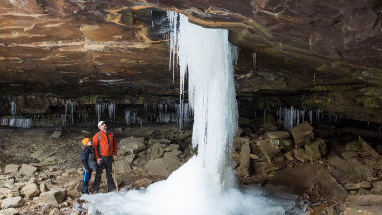 A father and son stand beneath a huge, frozen waterfall at Glory Hole Falls.