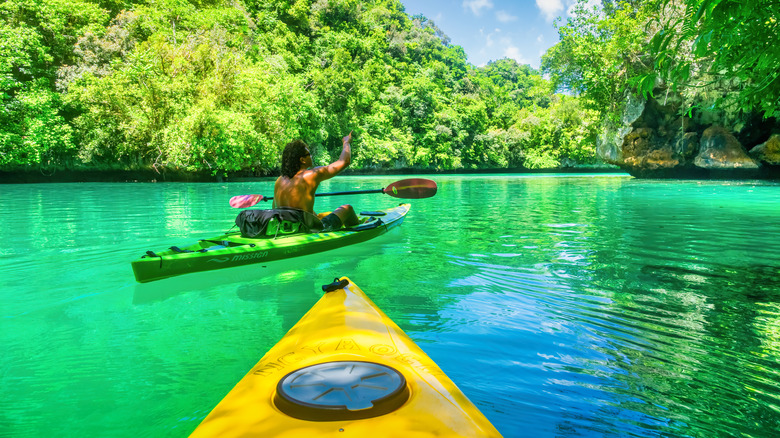 A tour guide in green kayak leads a vistor in a yellow kayak around the Rock Islands of Palau