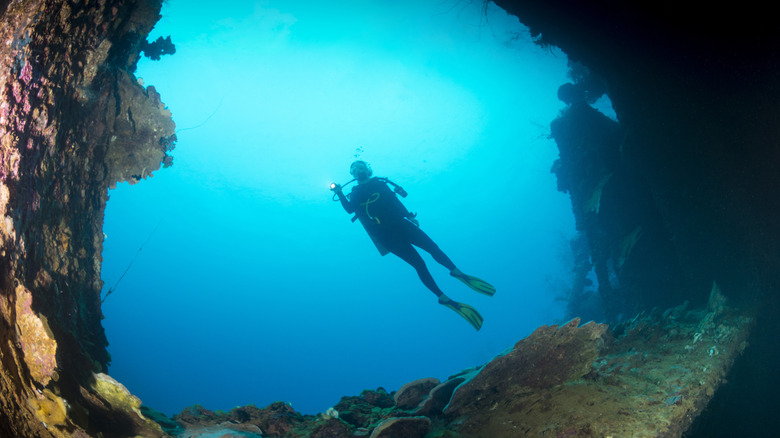 A scuba diver swims through the hole of shipwreck encrusted with coral in Palau