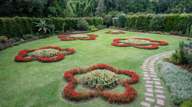A green ornamental lawn features flower beds shaped like red flowers with yellow centers