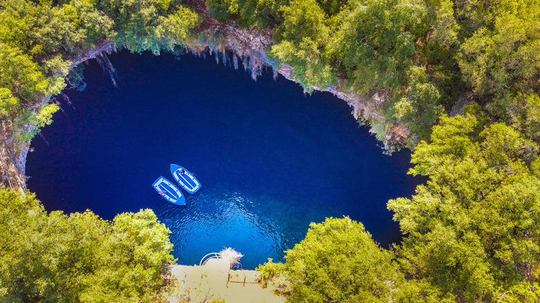 Drone view of Melissani cave lake in Sami, Kefalonia, Greece, with lush forests, turquoise waters, and boats