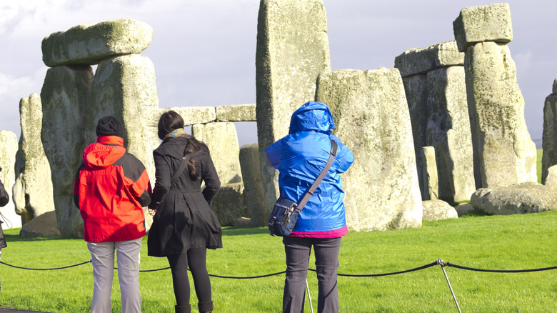 People taking photos of Stonehenge from the walking path behind a rope barrier