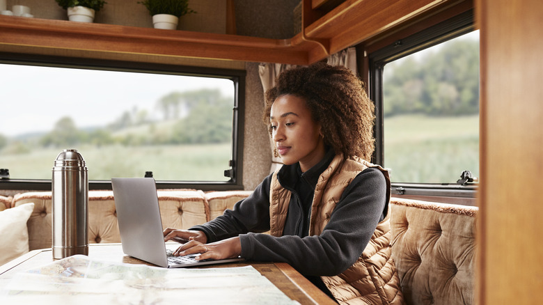 a woman in a camper van sitting at her laptop with nature views out the windows