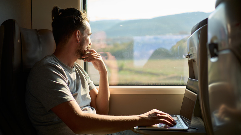 Man with laptop looking out a train window