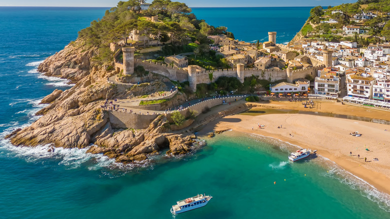 A Spanish beach with clear water and a town behind
