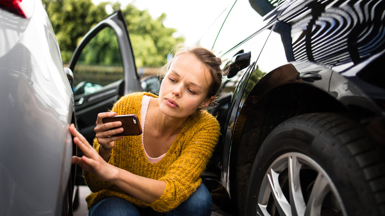 Woman holding phone and inspecting car for damage